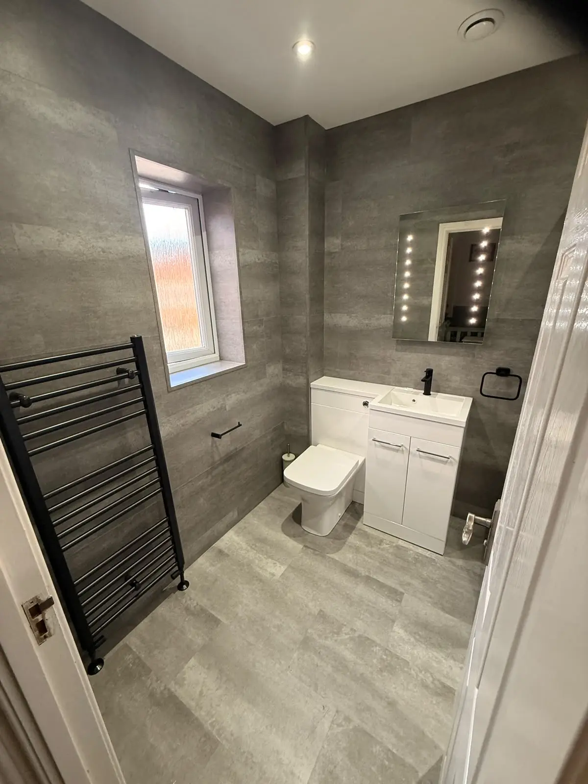 Chester-le-Street bathroom with medium-grey SPC walls, combi toilet–vanity unit, LED mirror and black towel rail